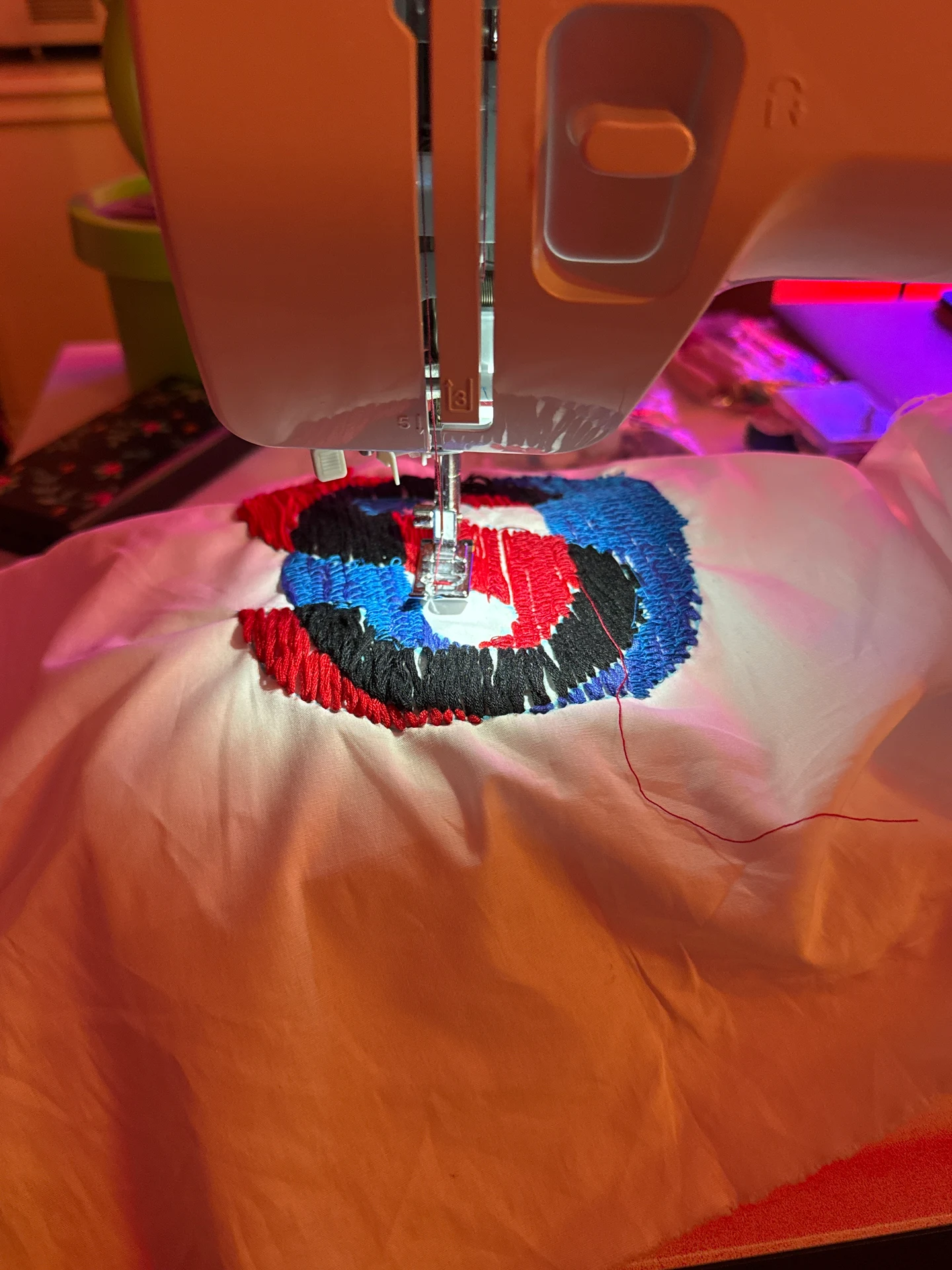 An embroidery machine stitching colored letterforms into fabric.
